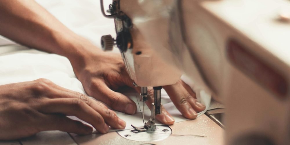 Close-up of hands using a sewing machine, depicting craftsmanship and textiles indoors.